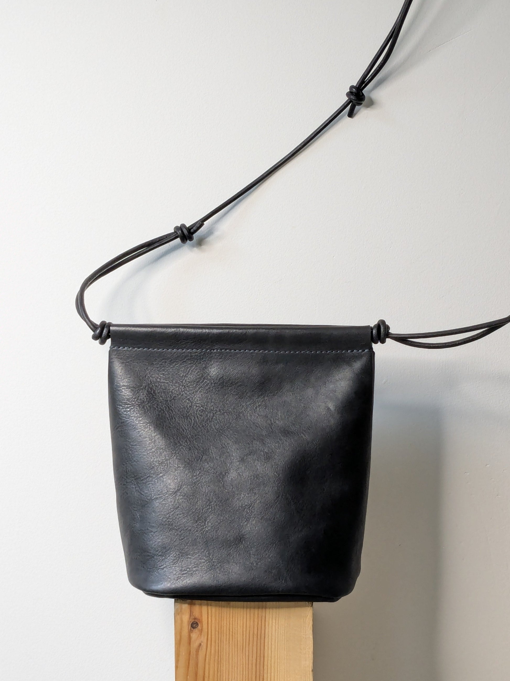 Black leather bag with a strap on a wooden block against a light gray background