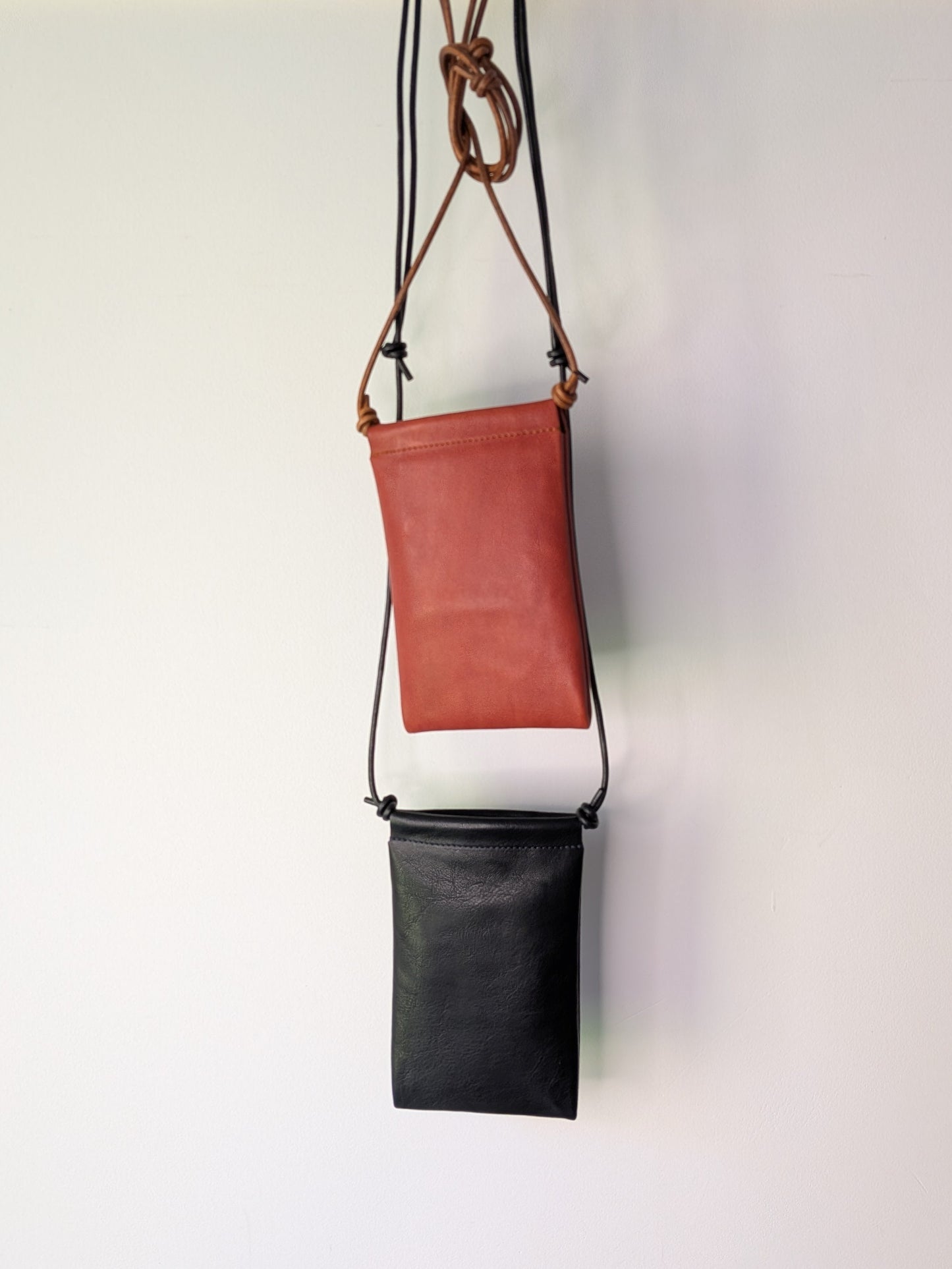 Two leather bags, one brown and one black, hanging on a wooden rod against a white background.