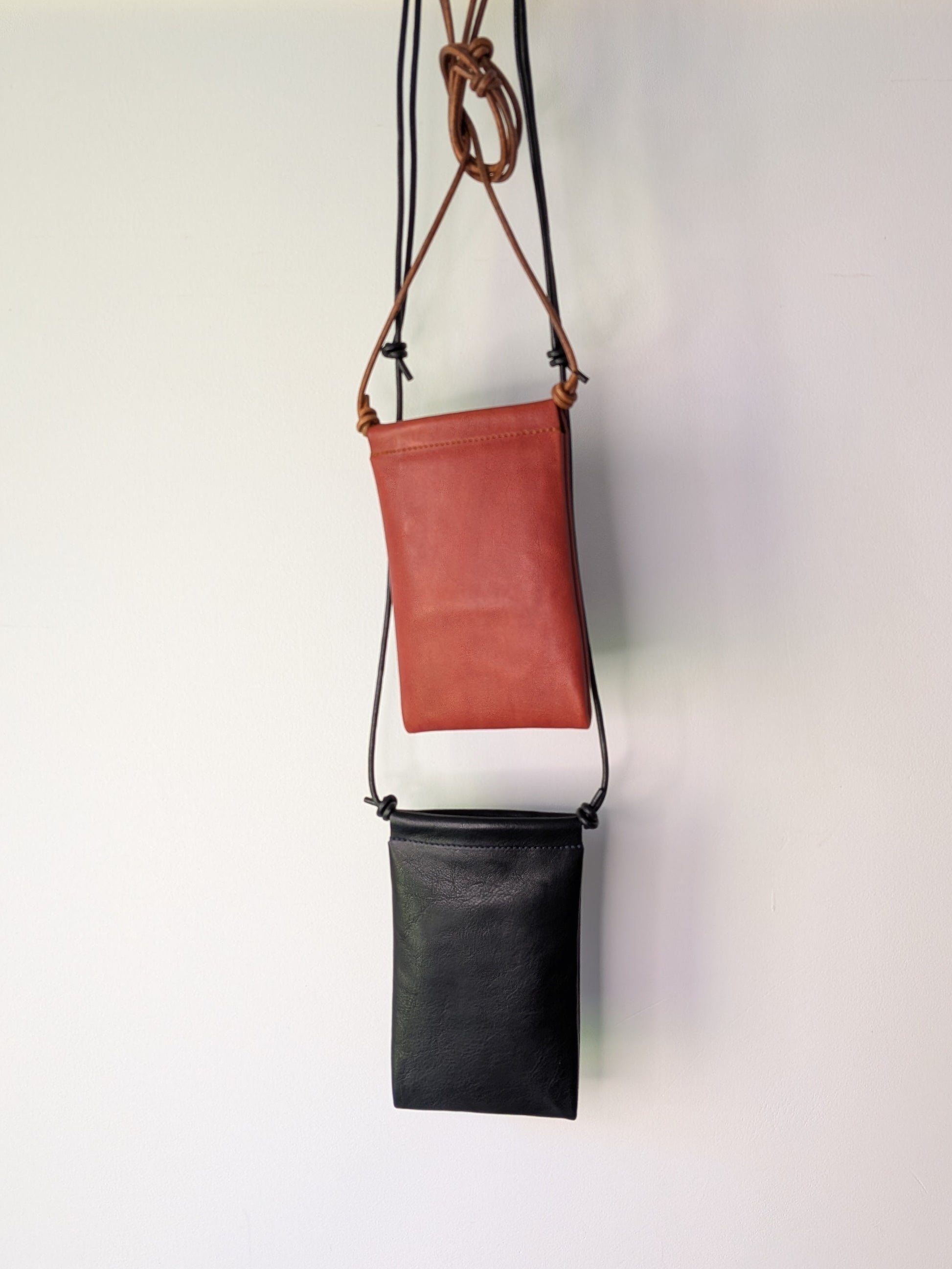 Two leather bags, one brown and one black, hanging on a wooden rod against a white background.