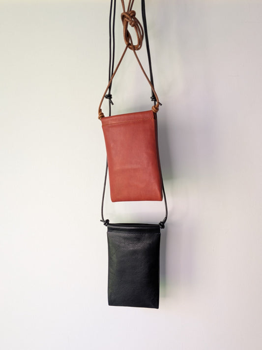 Two leather bags, one brown and one black, hanging on a wooden rod against a white background.
