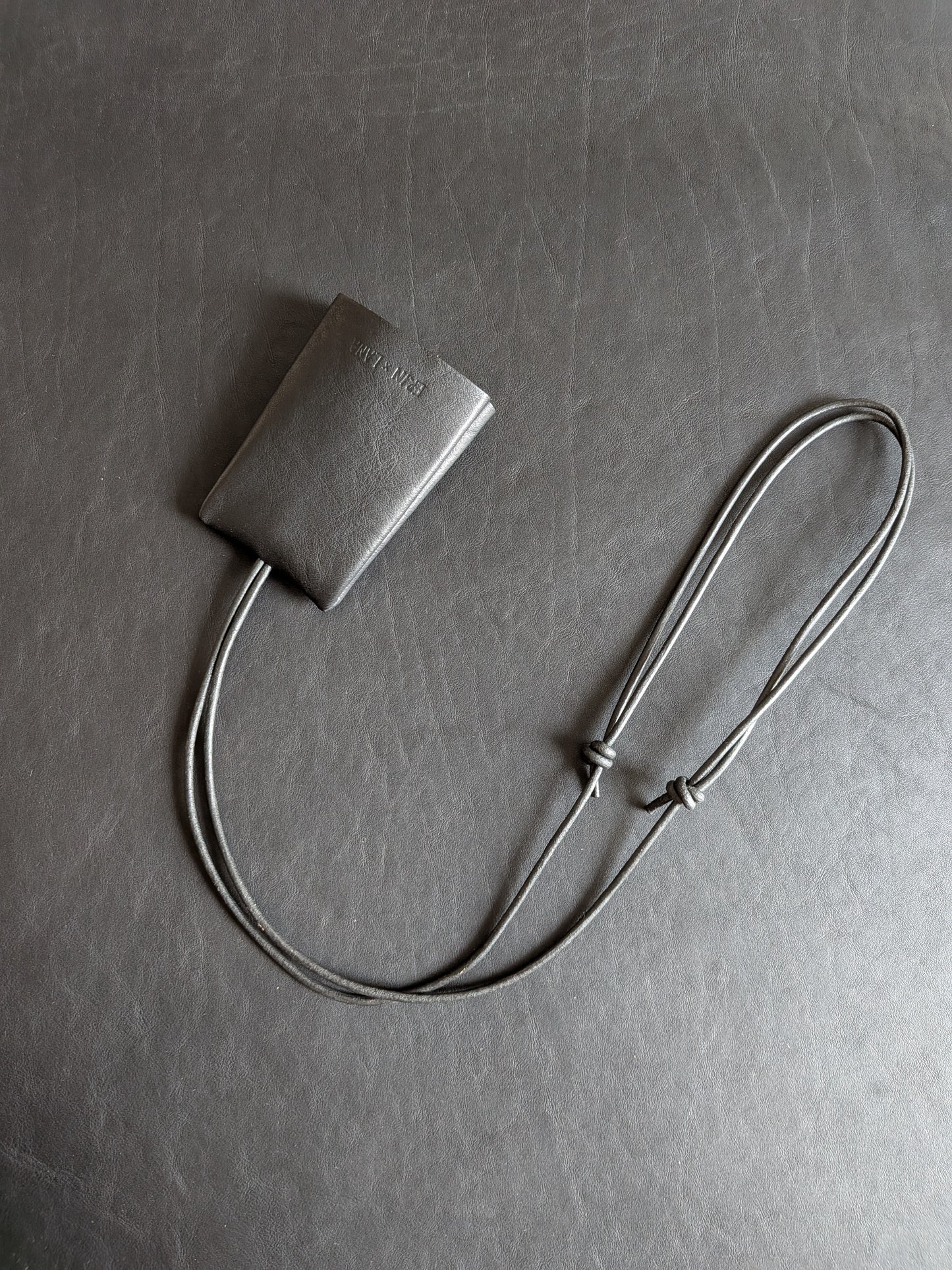 Small black leather pouch with a strap on a textured black leather background