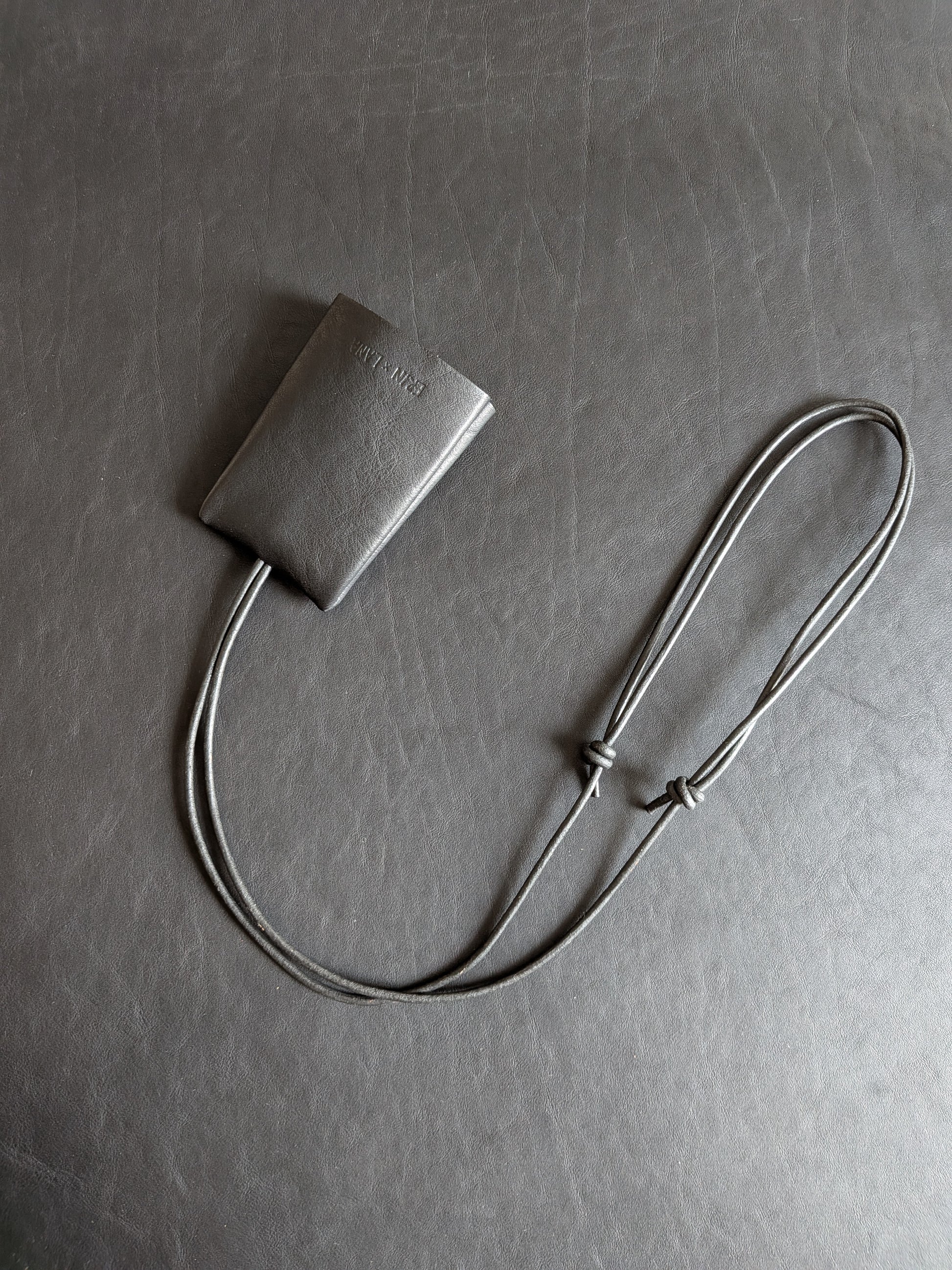 Small black leather pouch with a strap on a textured black leather background