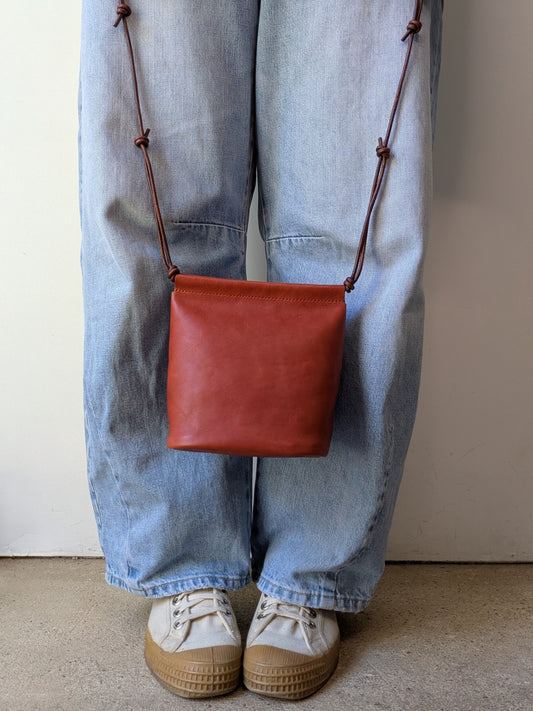 Person wearing a red leather bag over one shoulder with blue jeans and beige shoes.