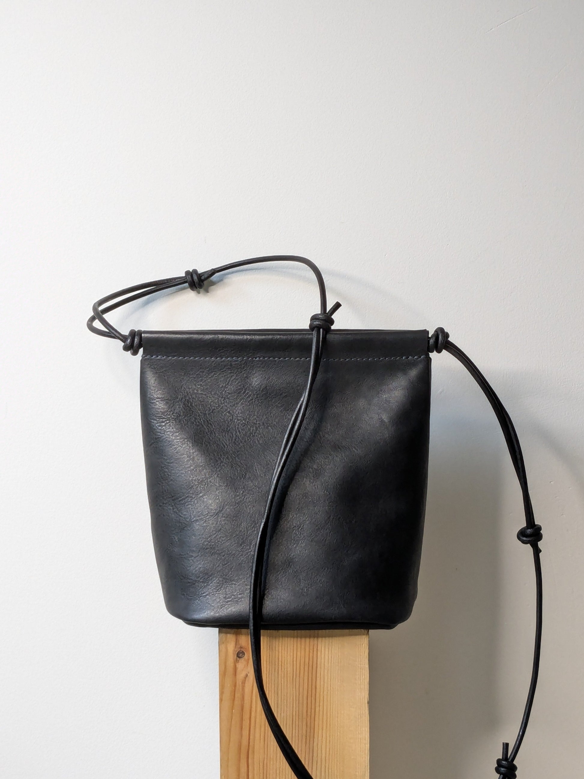 Black leather bag with a strap on a wooden block against a light gray background