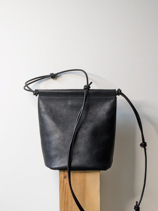 Black leather bag with a strap on a wooden block against a light gray background