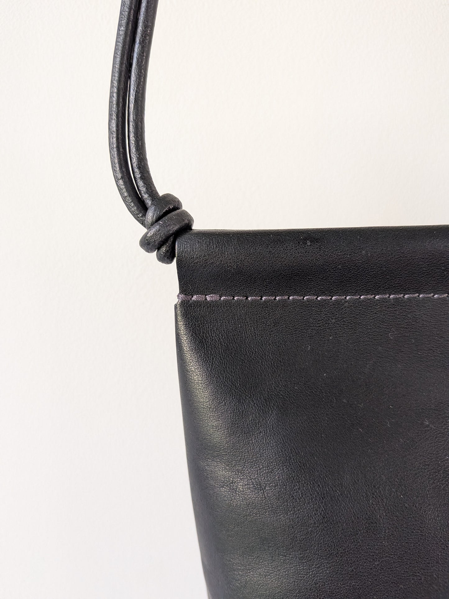 Close-up of a black leather handbag with a strap on a white background