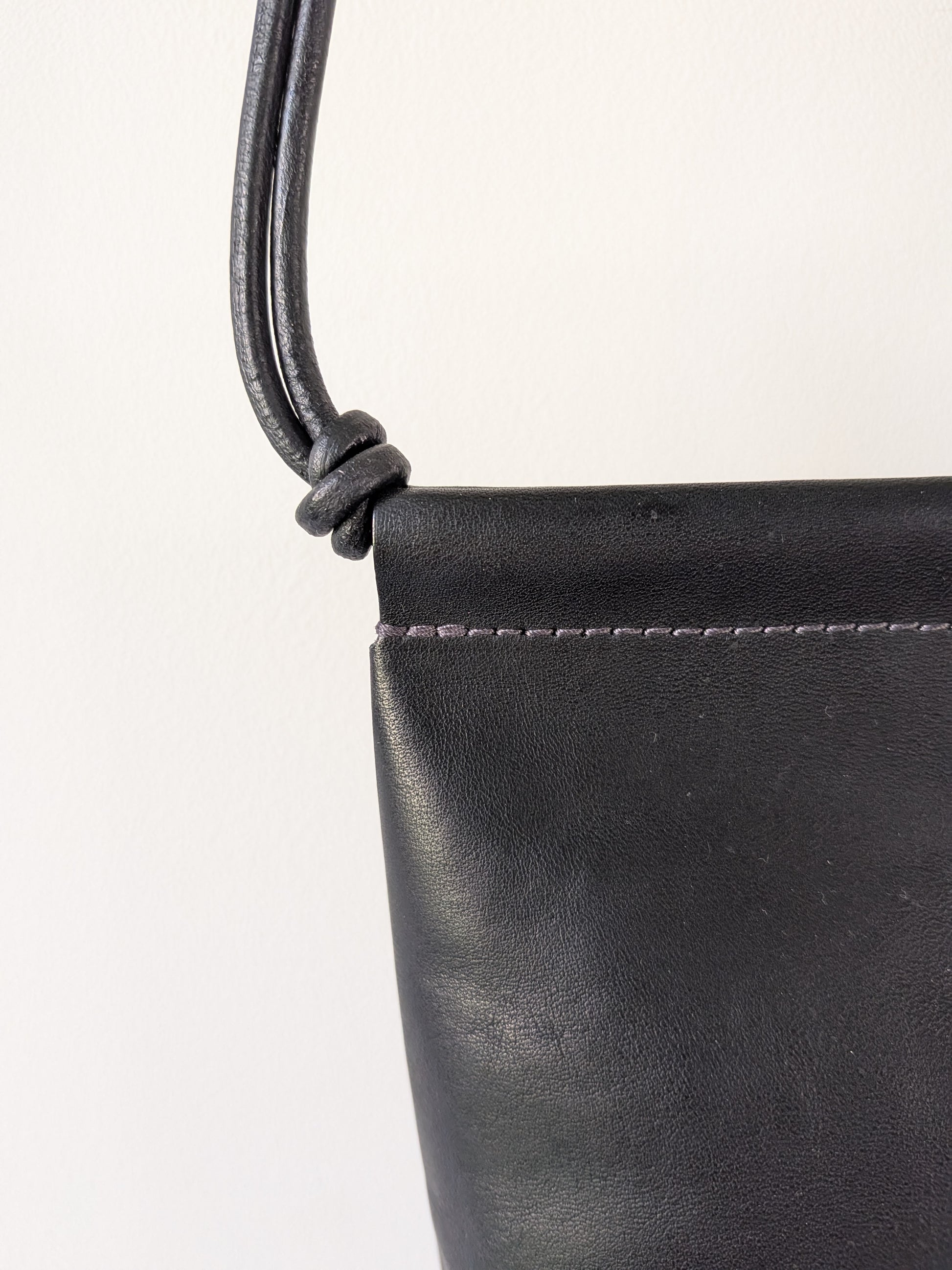 Close-up of a black leather handbag with a strap on a white background