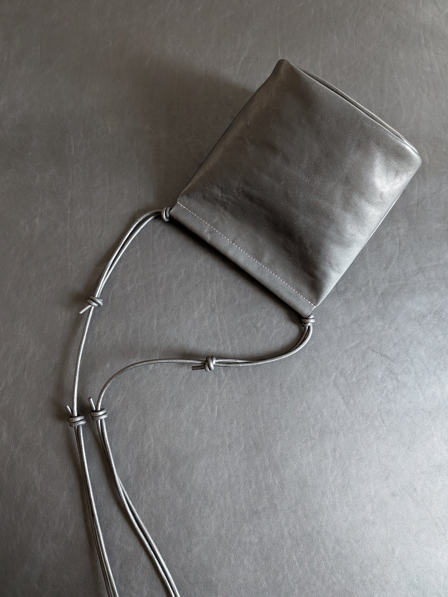 Black leather pouch with a strap on a black leather background