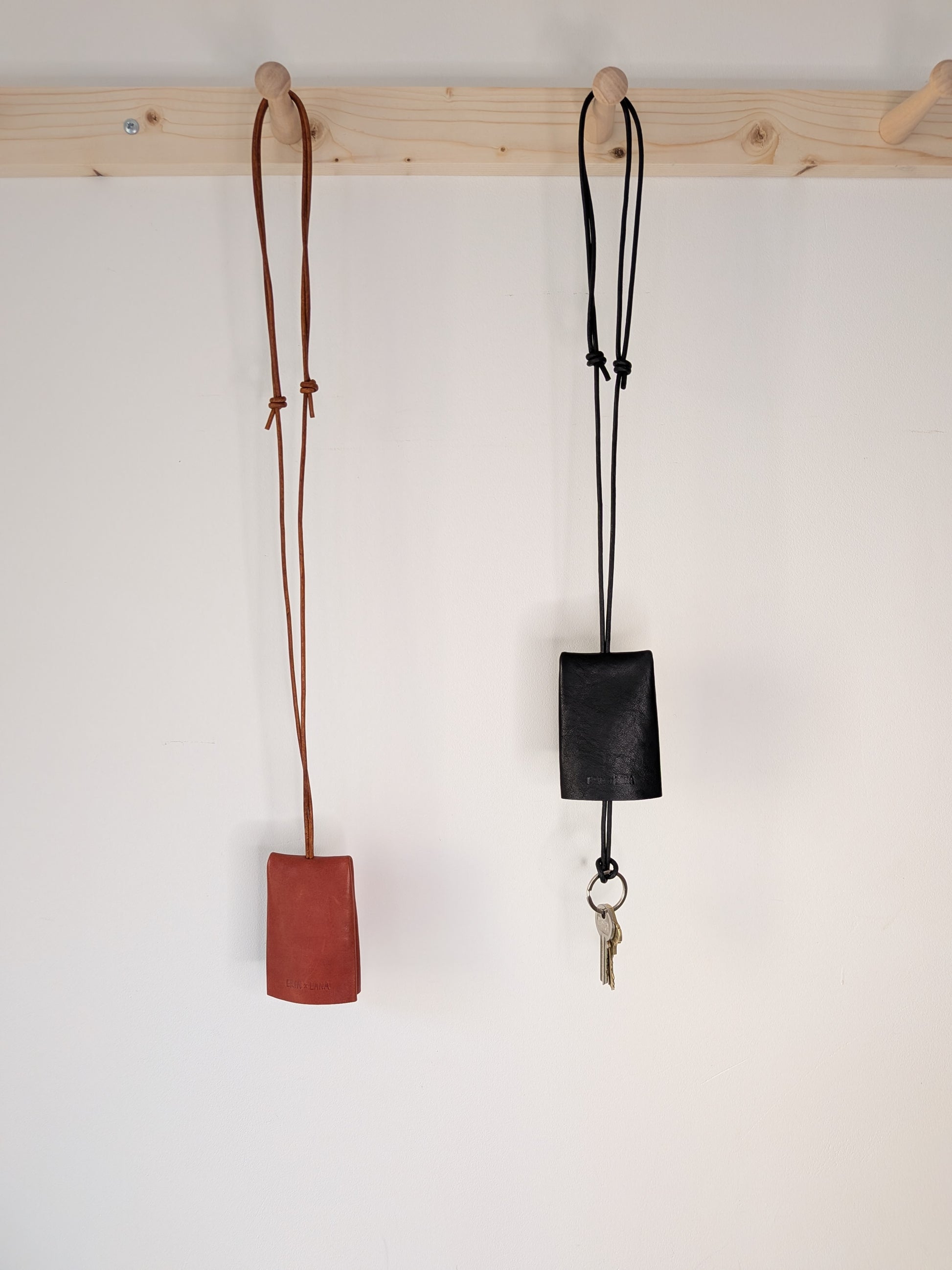 Two leather lanyards, one brown
 and one black, hanging on a wooden rack against a white wall.