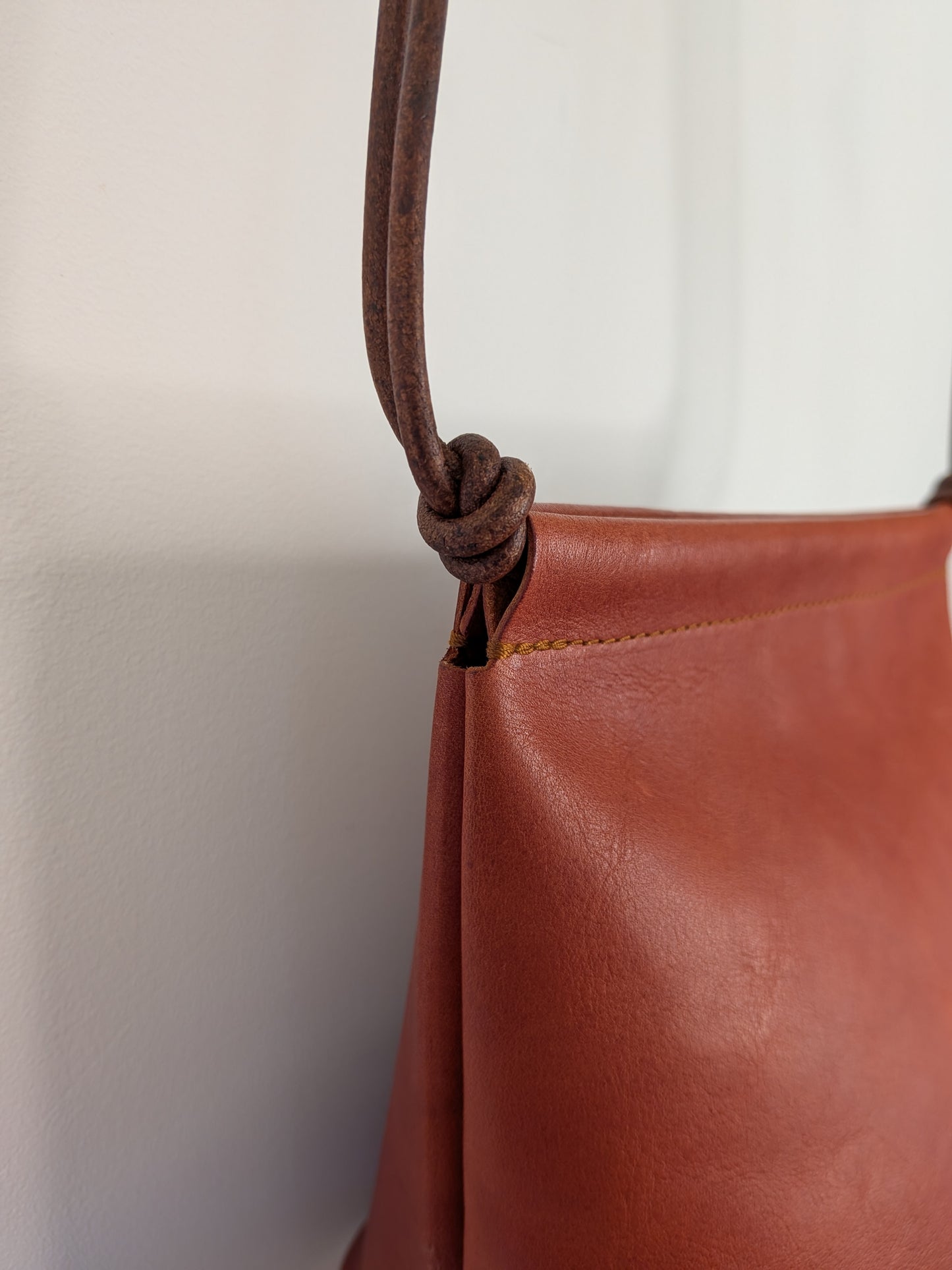 Close-up of a brown leather handbag with a knotted handle against a white background