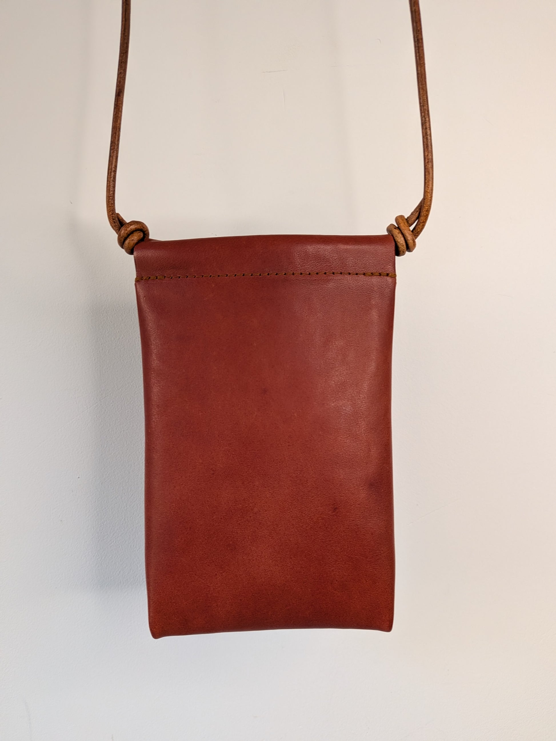 Brown leather phone pouch with a strap on a light  background